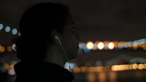 Woman wearing earphones takes off her hood at night