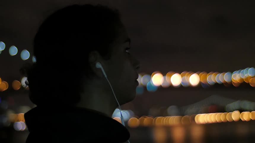Woman wearing earphones takes off her hood at night