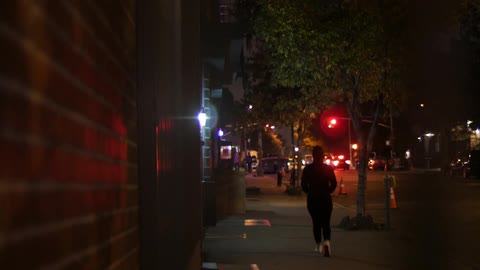 A pedestrian walks down a city street at night