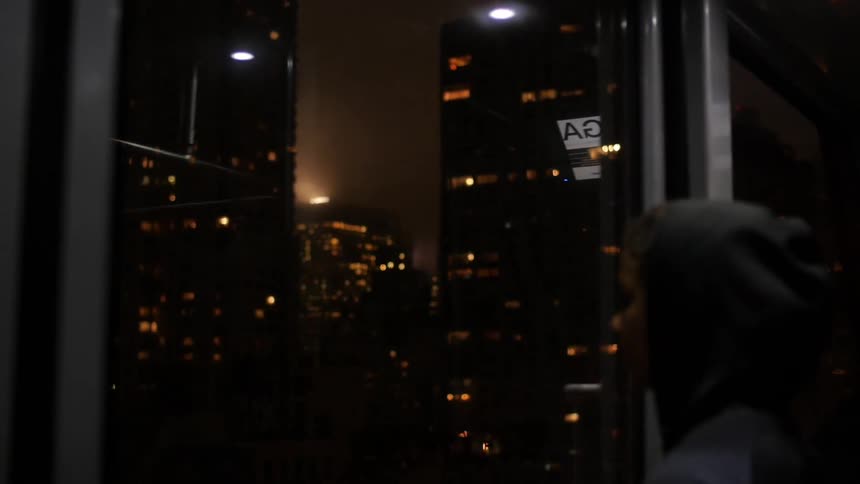 A woman looks out a window at a city at night