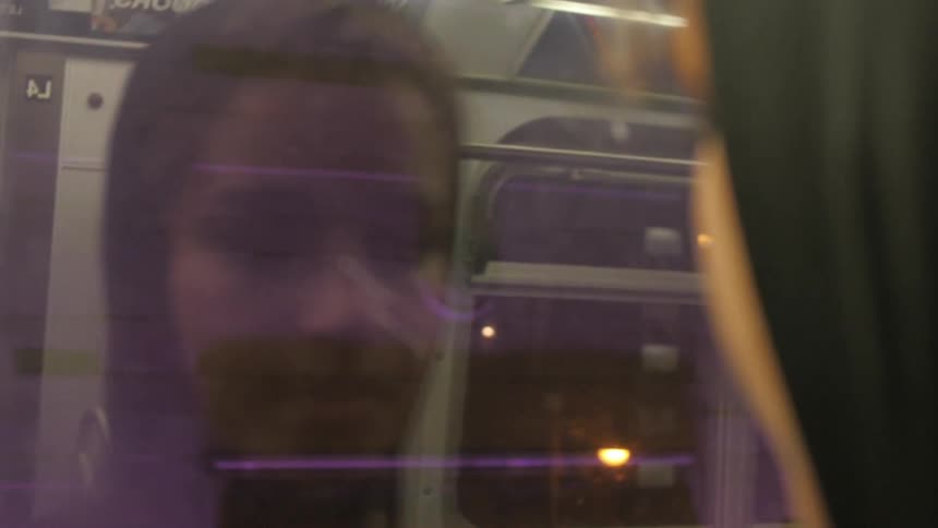 Hooded person looking through their reflection of a subway window in a city