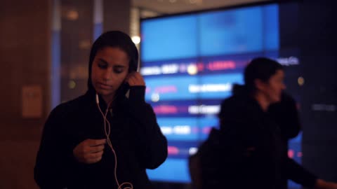 A woman puts in earbuds while people walk behind her