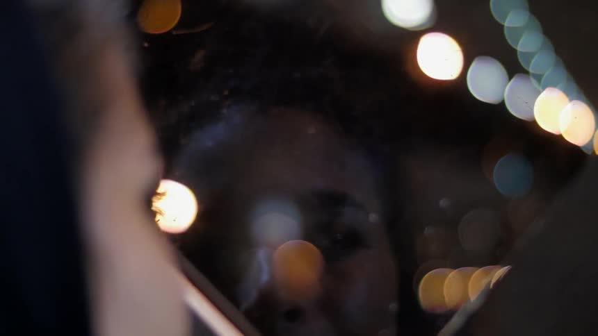 A woman looks out a window at the nighttime city skyline