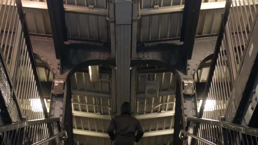 Person in a black, hooded jacket jogs up metal stairs