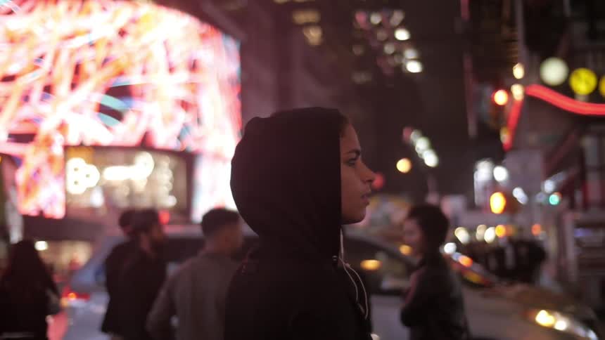 A woman standing on a city street surrounded by people vehicles and buildings
