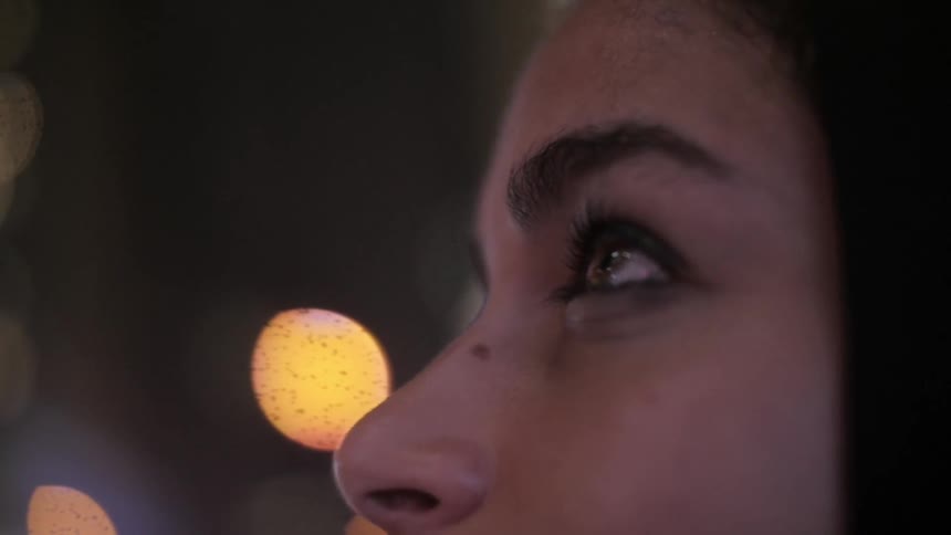 Close up of a womans face looking at flickering lights on a street at night