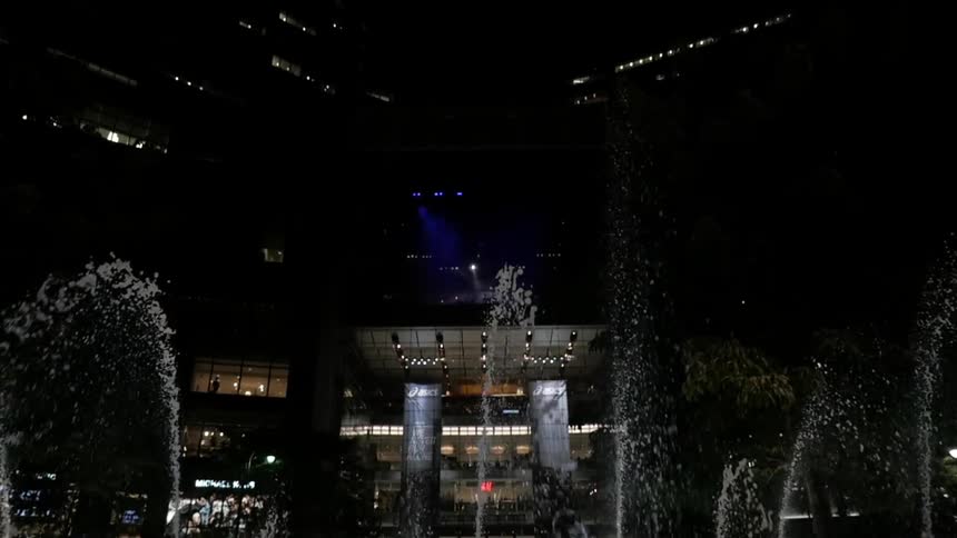 A water with multiple spouts is displayed in front of a city building