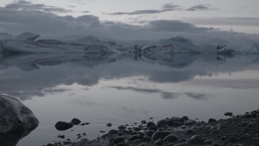 Rocks line the shimmering lake under a cloudy sky