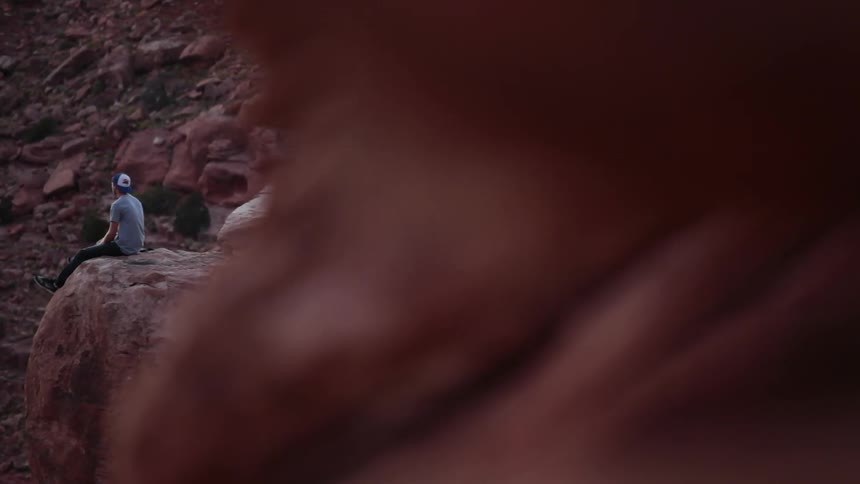 A man sits on the edge of a large boulder