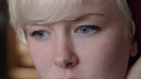 A close up of a young blonde woman with blue eyes watching something before looking down and away