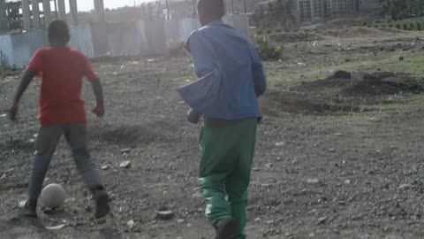 Boys playing kickball in the dirt on a cloudy day