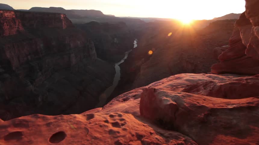 A large canyon with red colored mountains and a stream of water below during sunset