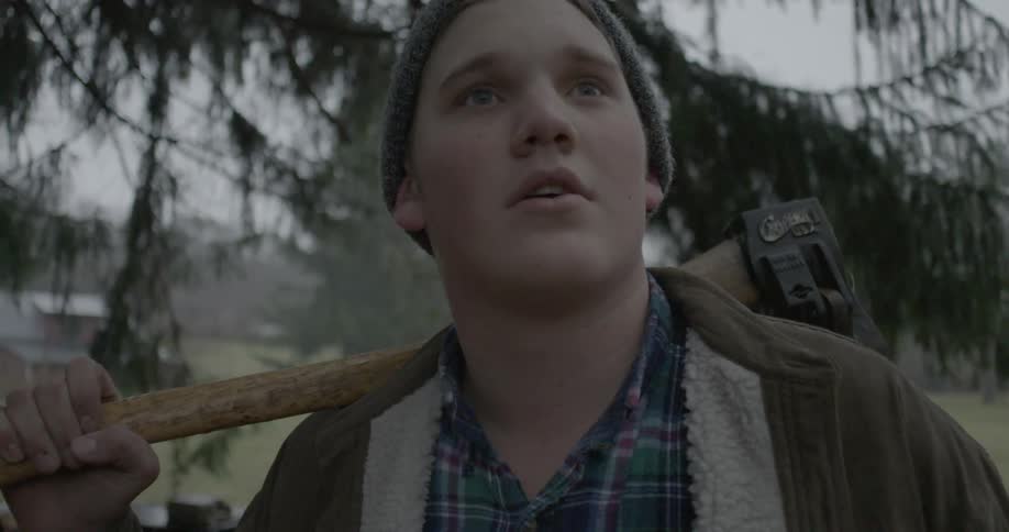 Lumberjack holds axe over his shoulder under the rain