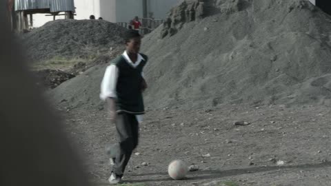 Black teenage boys play football in the dirt field