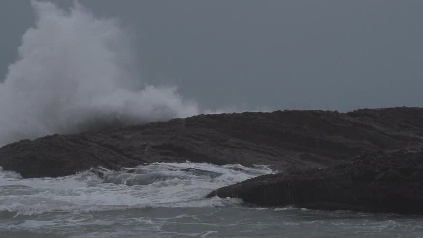 A large wave crashes on a rocky shore