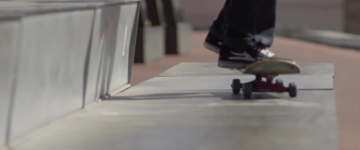 The feet of a person riding a skateboard down a concrete path on a sunny day