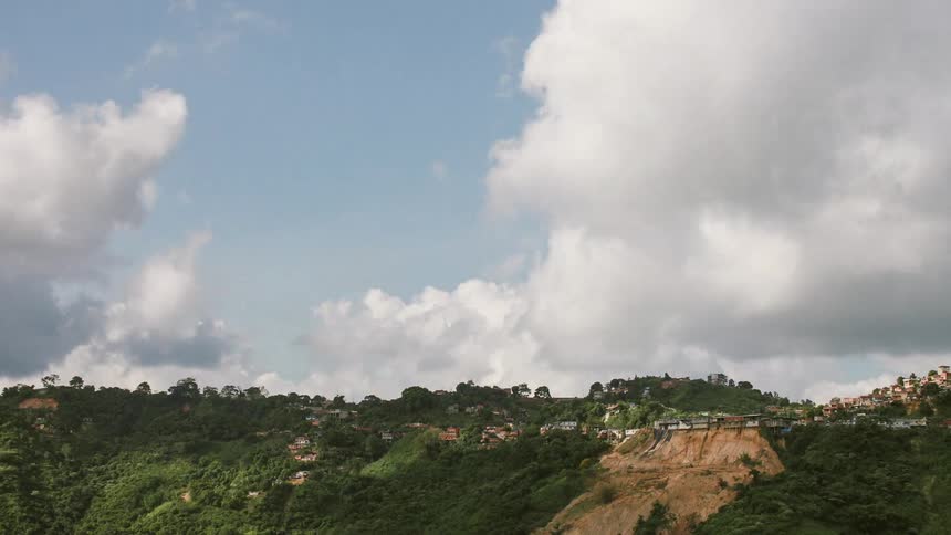 Clouds moving through a blue sky above a grassy and hilly area