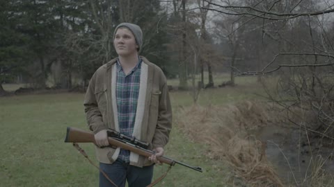 A man carrying a shotgun through the woods