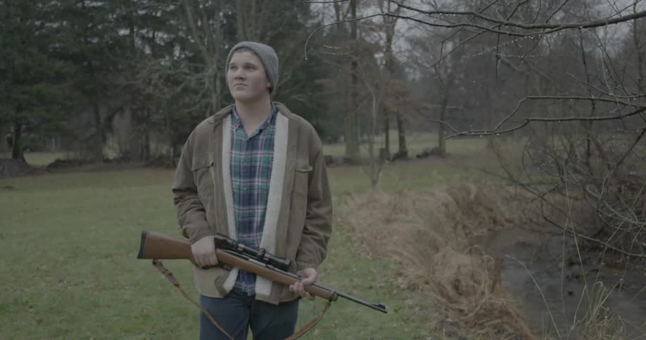 A man carrying a shotgun through the woods