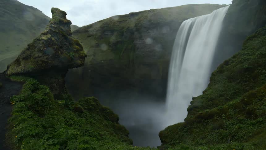 A waterfall pours into a lake beneath the large hills