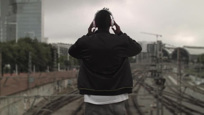 A man stands high above train tracks and puts head phones over his ears