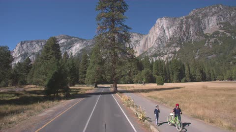 People walk down a sidewalk near a mountain