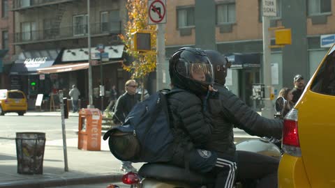 Two people ride a scooter in a city