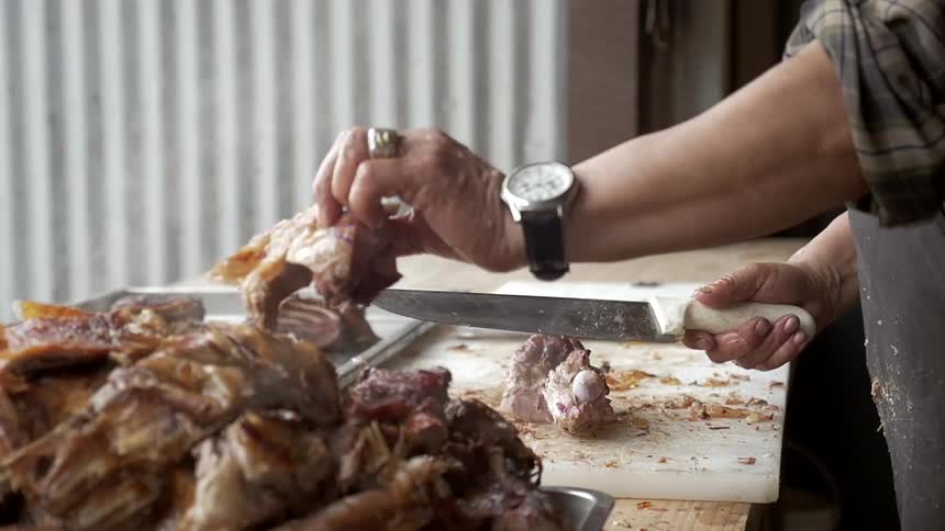 A man cuts a piece of cooked of meat with a large knife