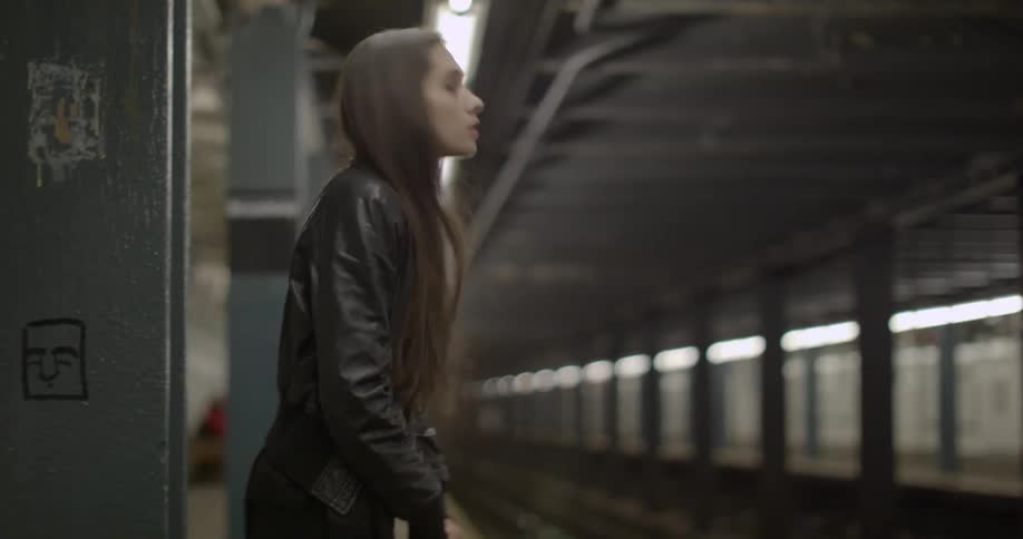 A woman stands at a subway station waiting for a train