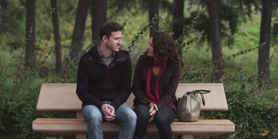 A man and a woman sitting and chatting on a park bench on a chilly day