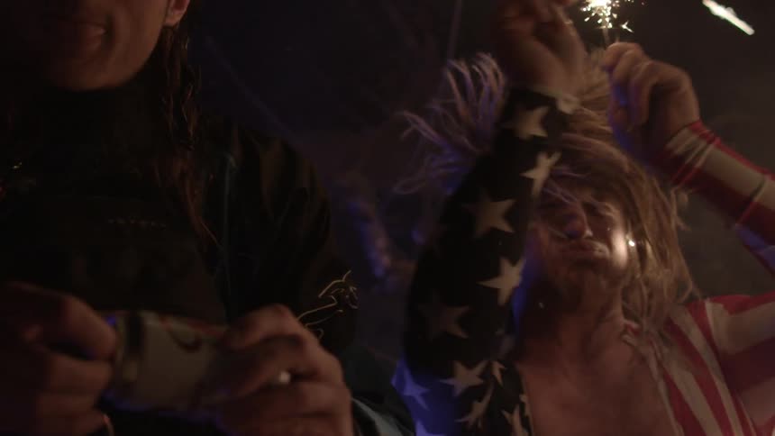 Two men outside at night one is holding sparklers and one is holding a can