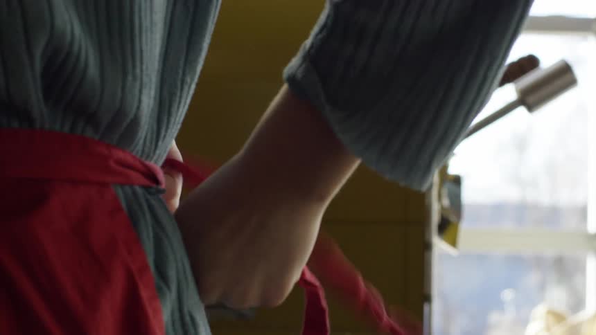 A person ties a red apron behind their back
