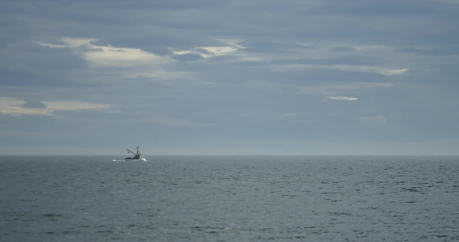 A boat travelling on the wide-open ocean under a cloudy sky