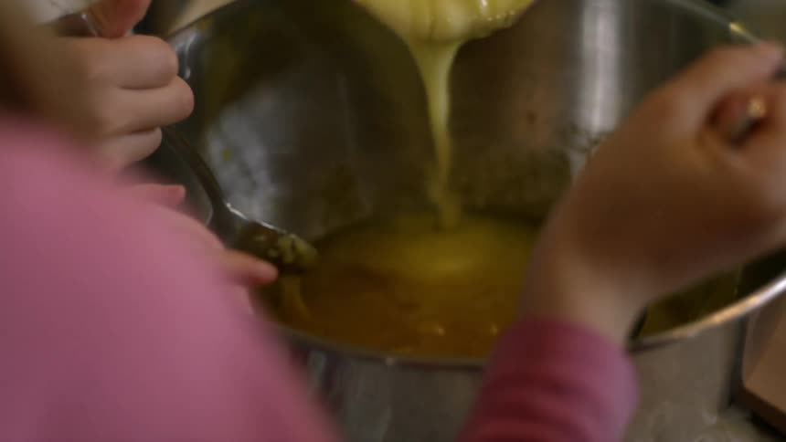 Two people mix some food in a silver bowl
