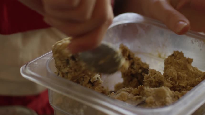 A woman is spooning out cookie dough for a small bakery