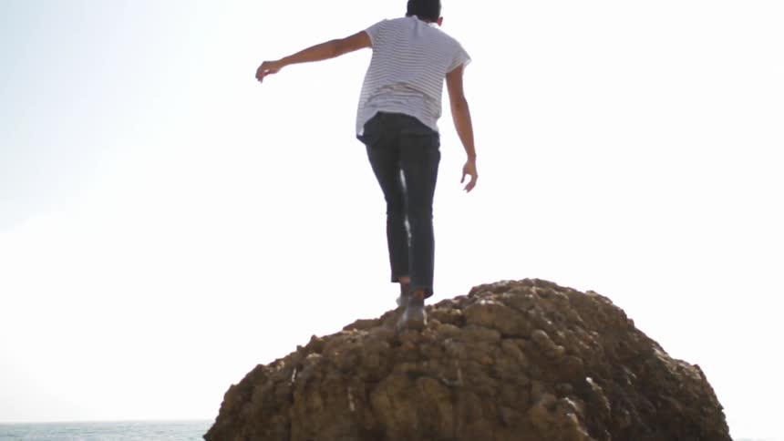 A man climbs up a large rock formation to get a view of the ocean