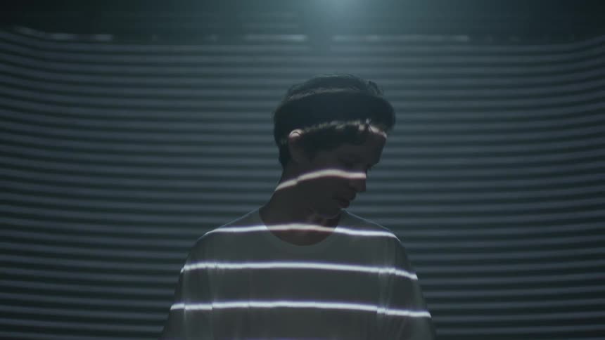 A man stands looking to the side as light reflects off his face and body