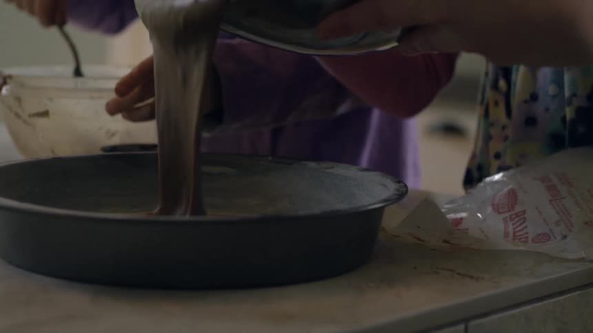 One person stirring a mixture in a bowl as another pours a mixture into a pan