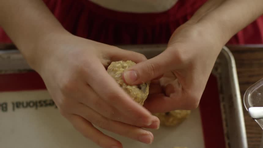 A woman spoons out and shapes cookie dough in a small bakery