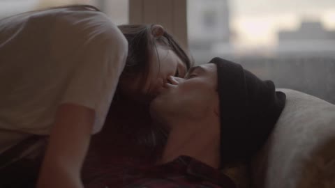 A young man and woman fall onto a couch to kiss