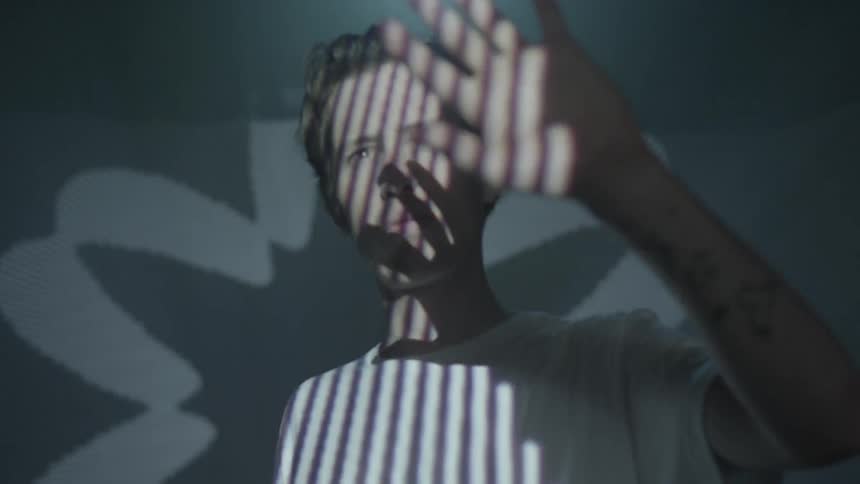 A man stares at his hands while bright light shines shapes and patterns at him