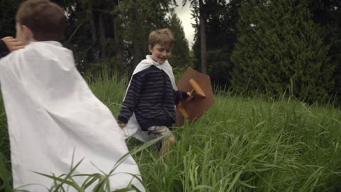Two young boys sword fight in a grassy area