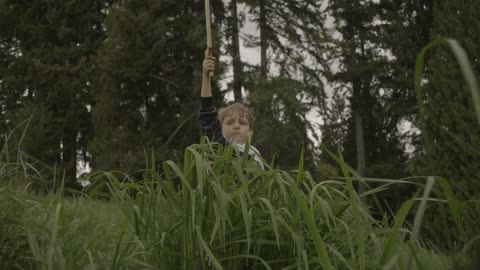 Young boy jumps up from behind the weeds holding a sword in the air