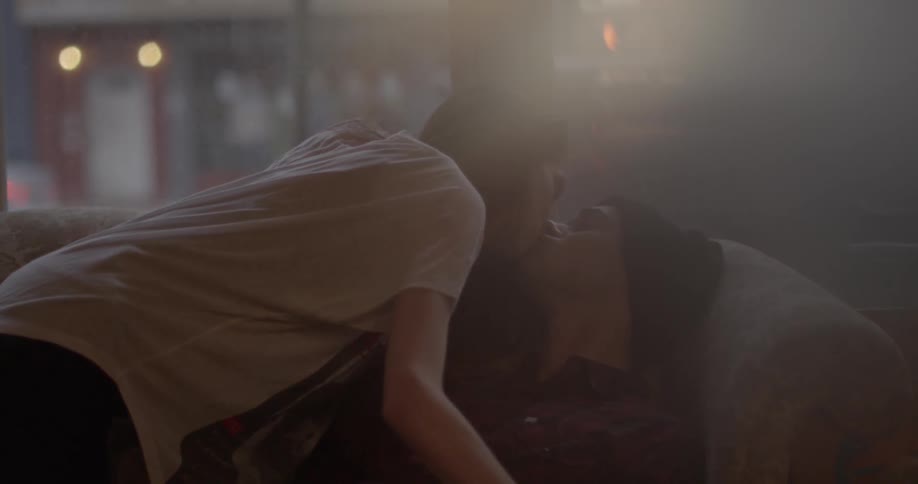 A woman kisses a man sitting on a sofa