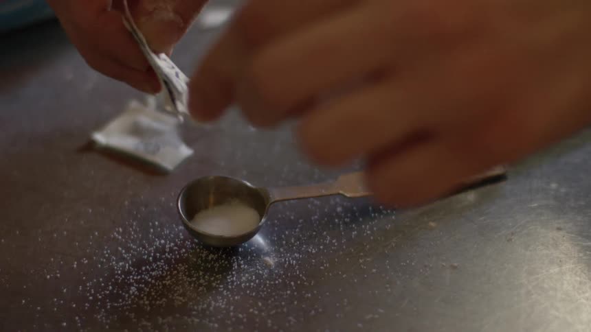 A person empties a sugar substitute packet into a measuring spoon