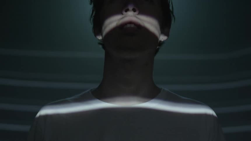 A person in the dark, then a series of horizontal lights falls across their face and shoulders