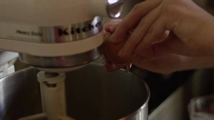 An egg is cracked into a stand mixer