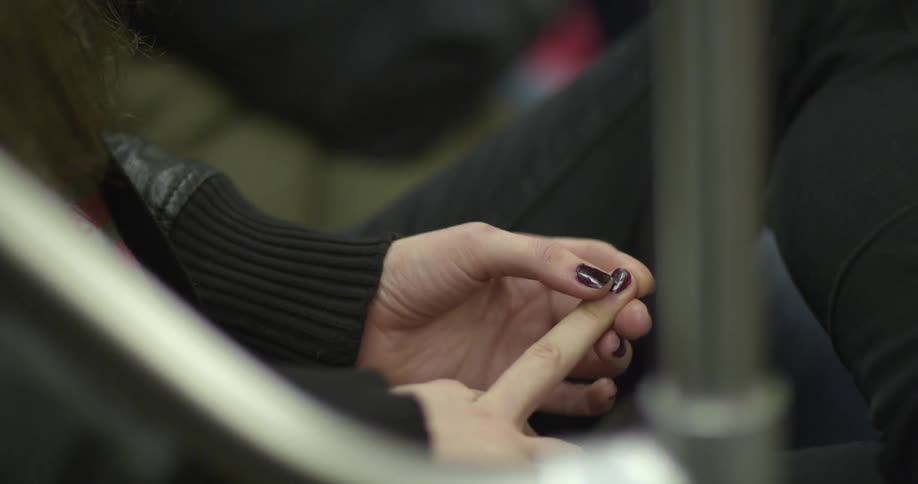 While sitting, a woman stares absentmindedly down at her painted fingernails