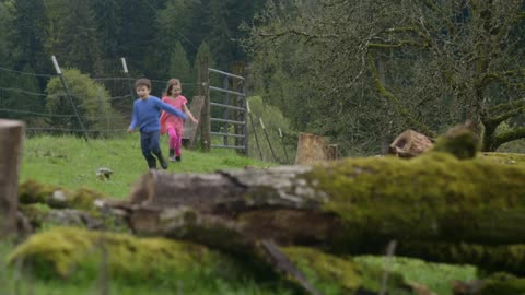 Two kids run outside near a fence
