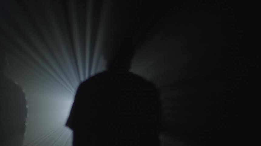 Three people are silhouetted by a bright light in the distance
